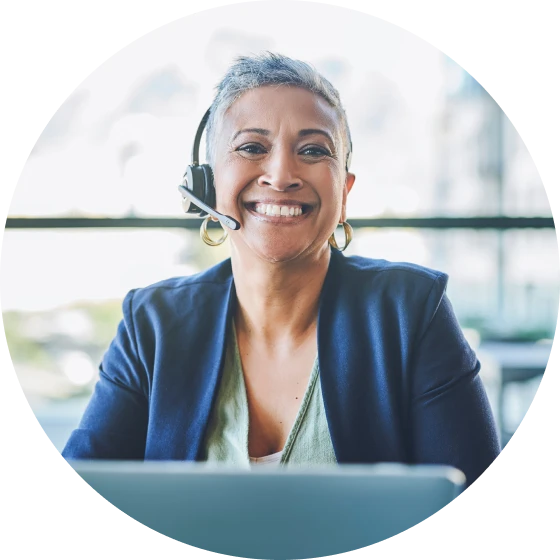 Patient Case Manager wearing telephone headset, seated behind laptop, smiling into camera
