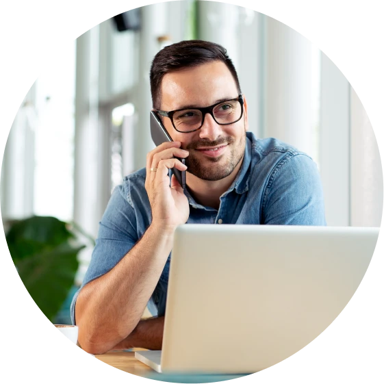 Man smiling on telephone, seated behind laptop computer