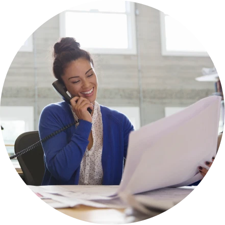 Woman in business casual attire, seated at table reviewing papers while talking on telephone